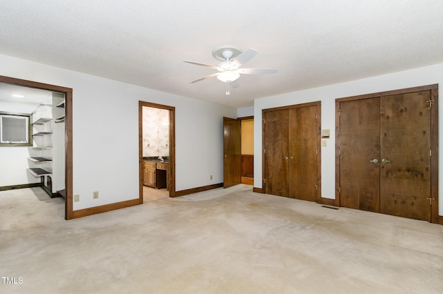 unfurnished bedroom featuring ensuite bathroom, light colored carpet, visible vents, baseboards, and two closets