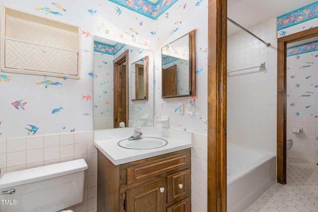 bathroom with wallpapered walls, toilet, tile patterned flooring, vanity, and tile walls