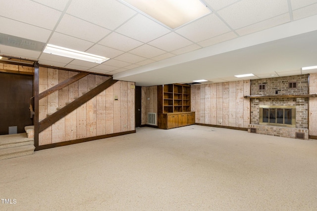 finished basement with wooden walls, visible vents, a drop ceiling, stairway, and a fireplace