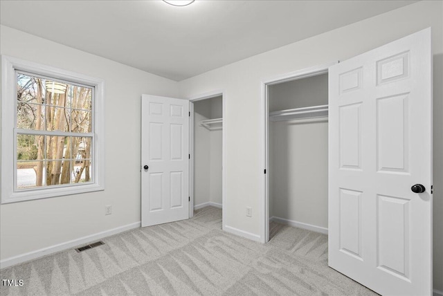 unfurnished bedroom with two closets, carpet flooring, visible vents, and baseboards