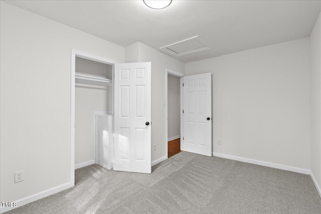 unfurnished bedroom with a closet, carpet flooring, attic access, and baseboards