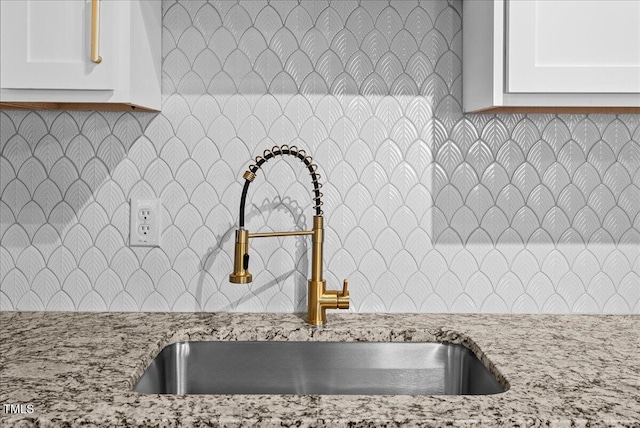 kitchen with light stone counters, a sink, white cabinets, and tasteful backsplash