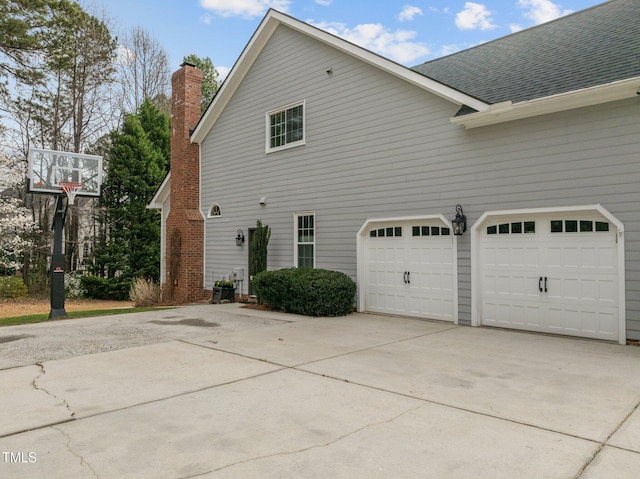 view of side of home featuring a garage, concrete driveway, a chimney, and a shingled roof