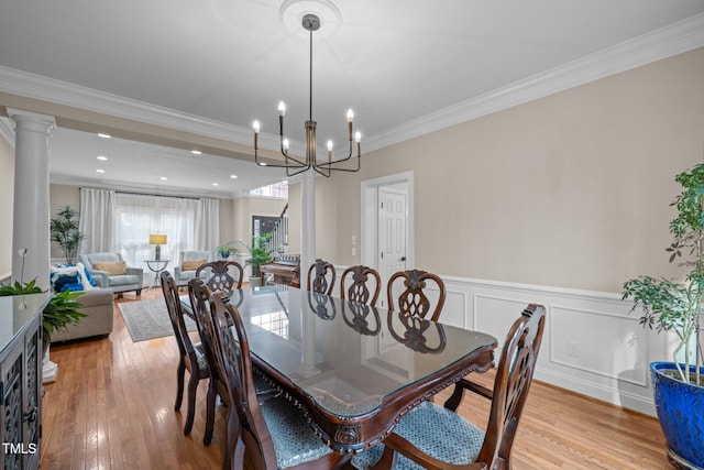 dining space with a wainscoted wall, light wood finished floors, an inviting chandelier, ornamental molding, and a decorative wall