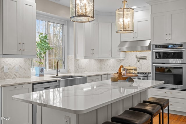 kitchen featuring a sink, decorative backsplash, appliances with stainless steel finishes, under cabinet range hood, and a kitchen breakfast bar