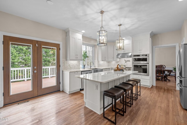 kitchen with under cabinet range hood, tasteful backsplash, appliances with stainless steel finishes, and light wood finished floors