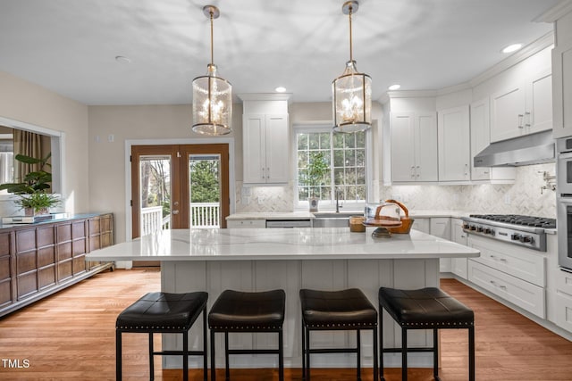 kitchen featuring light wood finished floors, white cabinets, under cabinet range hood, appliances with stainless steel finishes, and a kitchen breakfast bar