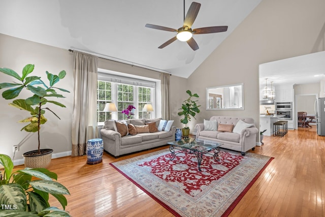 living area with baseboards, ceiling fan with notable chandelier, light wood-style floors, and high vaulted ceiling