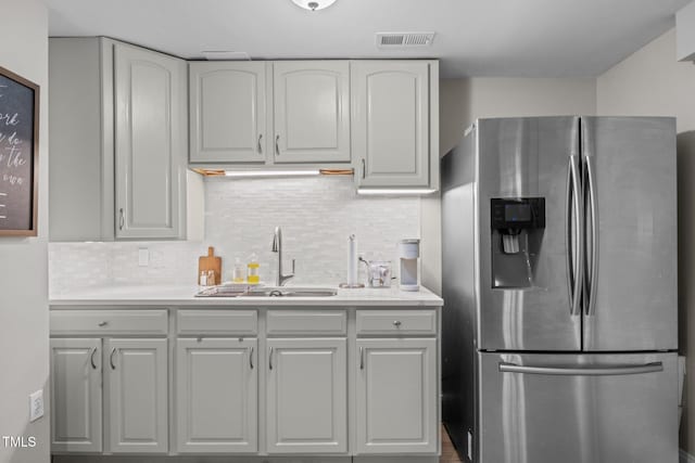 kitchen featuring visible vents, a sink, light countertops, stainless steel fridge, and backsplash