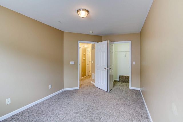 unfurnished bedroom with a closet, a spacious closet, baseboards, and carpet flooring