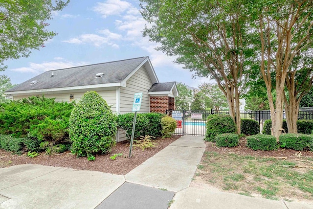 view of home's exterior with roof with shingles, fence, a pool, and brick siding