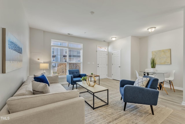 living room with light wood-style floors, visible vents, and baseboards