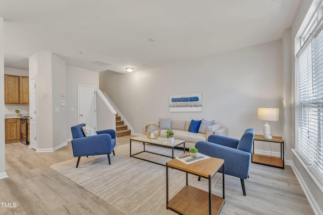 living area featuring light wood-style flooring, stairs, and baseboards