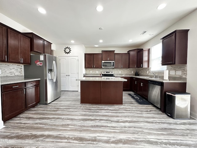 kitchen with dark brown cabinetry, visible vents, appliances with stainless steel finishes, a center island, and light wood-style floors