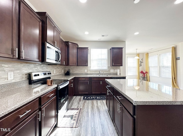 kitchen with a center island, light wood-style flooring, decorative backsplash, appliances with stainless steel finishes, and a sink