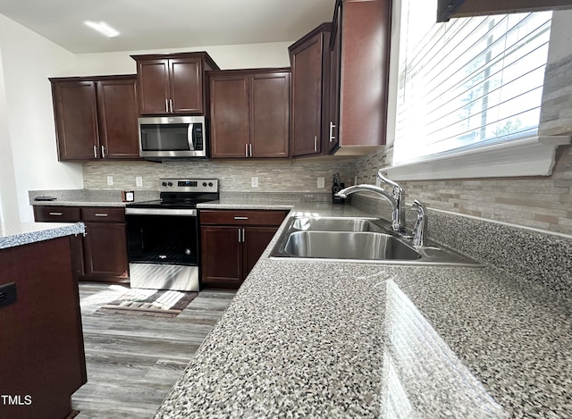 kitchen with wood finished floors, a sink, dark brown cabinets, appliances with stainless steel finishes, and decorative backsplash