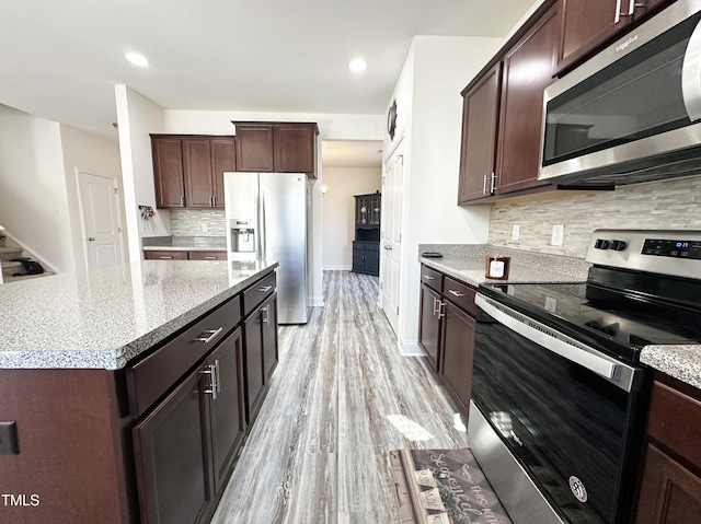 kitchen with stainless steel appliances, light wood finished floors, dark brown cabinets, and tasteful backsplash