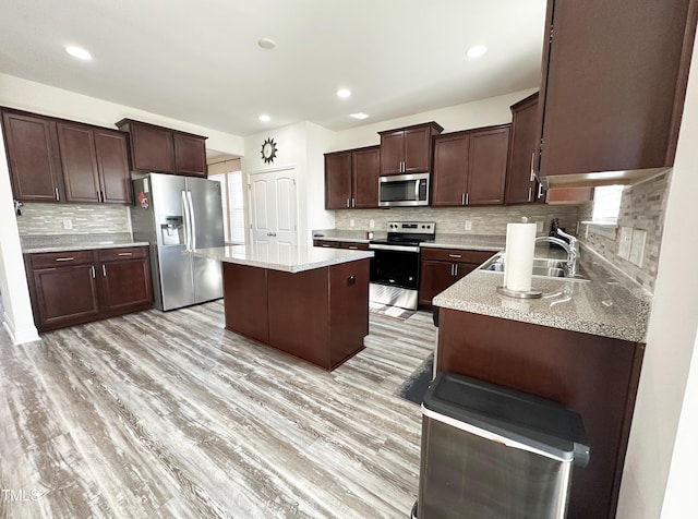 kitchen featuring dark brown cabinetry, stainless steel appliances, a sink, a center island, and light wood finished floors