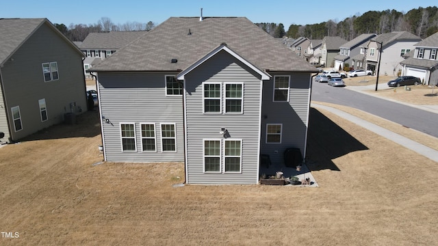 back of property featuring a shingled roof, a residential view, and a yard