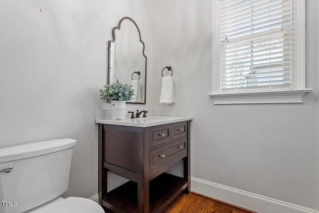 half bathroom featuring toilet, baseboards, wood finished floors, and vanity