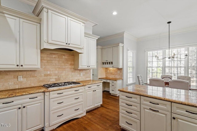 kitchen with light stone counters, a notable chandelier, stainless steel gas cooktop, ornamental molding, and backsplash