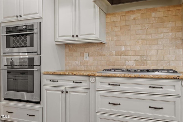 kitchen featuring stainless steel appliances, light stone counters, white cabinetry, and decorative backsplash