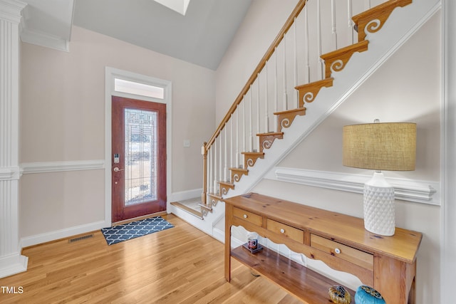 entrance foyer featuring baseboards, visible vents, lofted ceiling, wood finished floors, and stairs