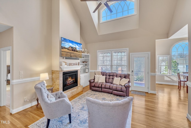 living room featuring a ceiling fan, baseboards, wood finished floors, and a glass covered fireplace