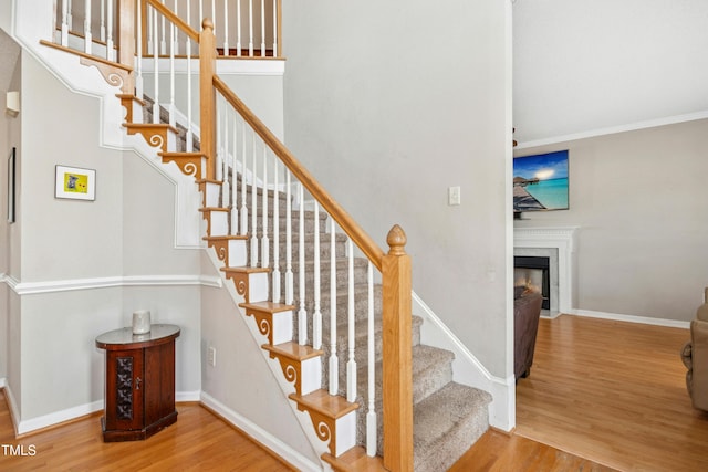 stairway with a fireplace with flush hearth, baseboards, wood finished floors, and ornamental molding