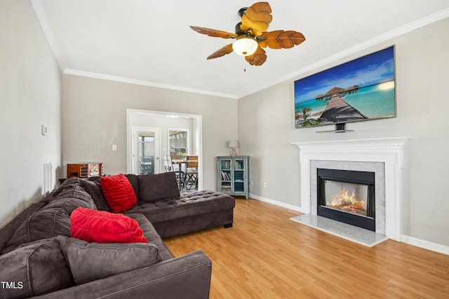 living area featuring light wood-style floors, a glass covered fireplace, crown molding, and baseboards