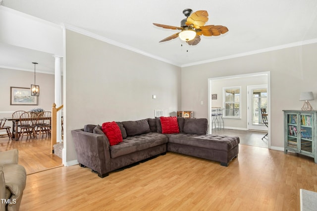 living room featuring ceiling fan with notable chandelier, crown molding, baseboards, light wood finished floors, and ornate columns