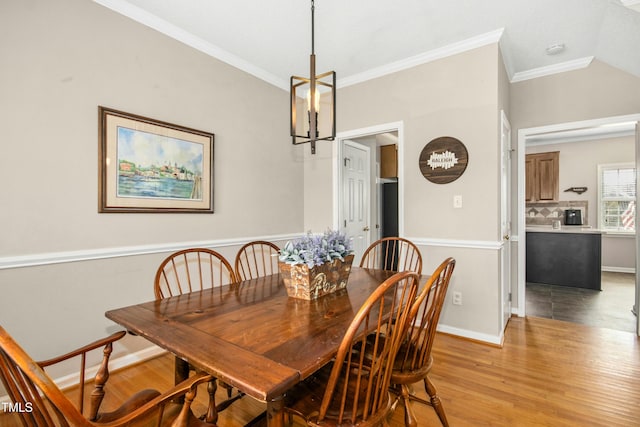 dining room featuring light wood-type flooring, vaulted ceiling, crown molding, and baseboards