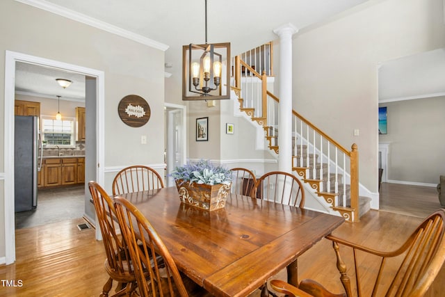 dining space featuring decorative columns, light wood-style flooring, stairs, and ornamental molding