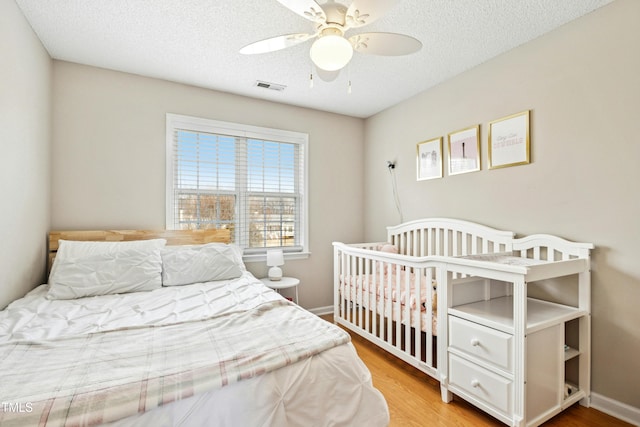 bedroom featuring baseboards, a textured ceiling, visible vents, and wood finished floors