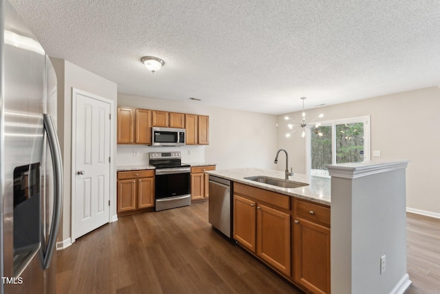 kitchen with dark wood-style flooring, brown cabinets, a center island with sink, appliances with stainless steel finishes, and a sink