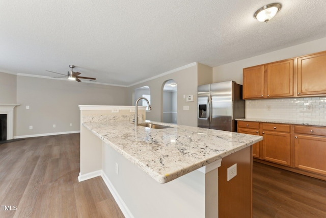 kitchen featuring dark wood finished floors, a fireplace, stainless steel refrigerator with ice dispenser, decorative backsplash, and a sink