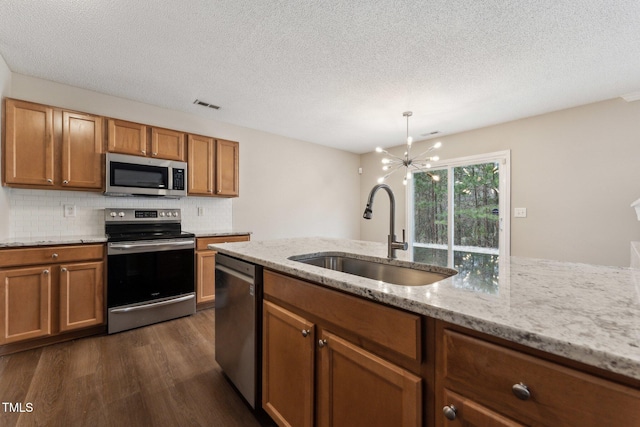 kitchen with brown cabinets, stainless steel appliances, visible vents, dark wood-type flooring, and a sink