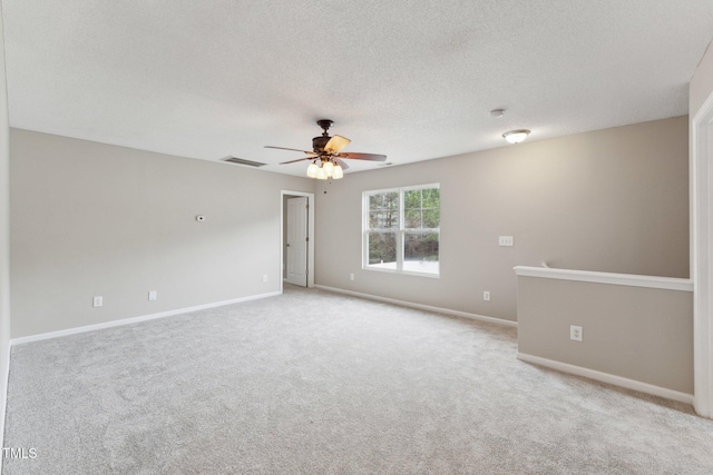 spare room featuring a textured ceiling, carpet floors, visible vents, a ceiling fan, and baseboards