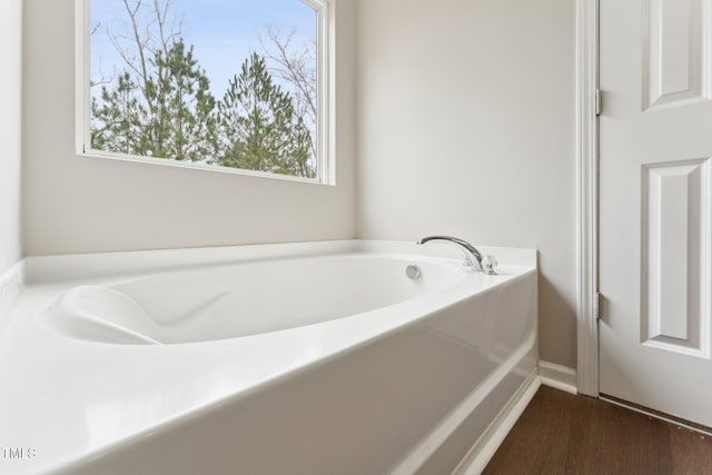 bathroom with wood finished floors, a garden tub, and baseboards