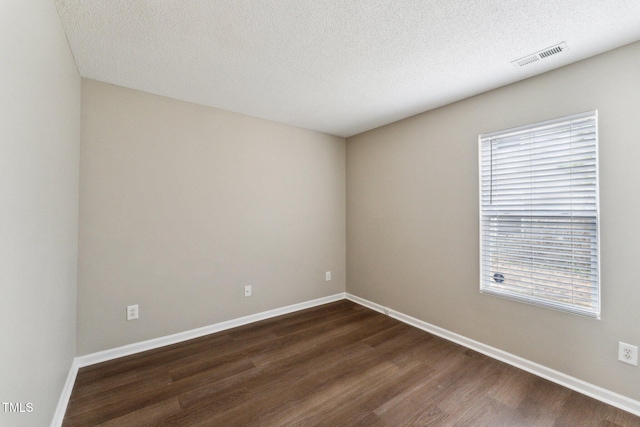 empty room featuring visible vents, dark wood finished floors, a textured ceiling, and baseboards