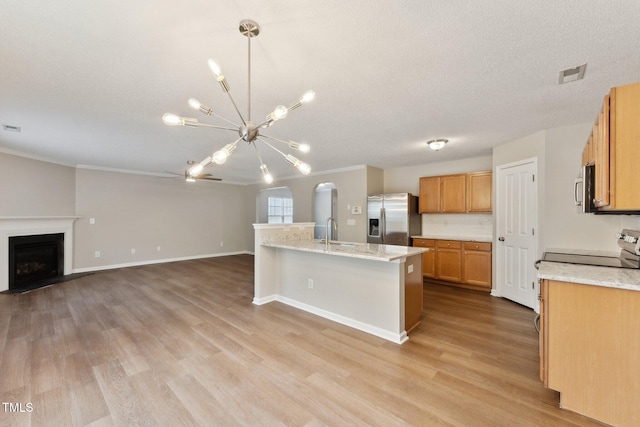 kitchen featuring appliances with stainless steel finishes, arched walkways, a fireplace, and light wood-style flooring