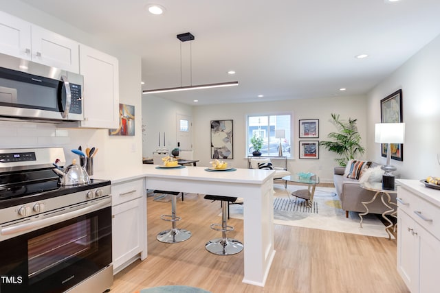 kitchen with light wood finished floors, light countertops, appliances with stainless steel finishes, white cabinetry, and a peninsula