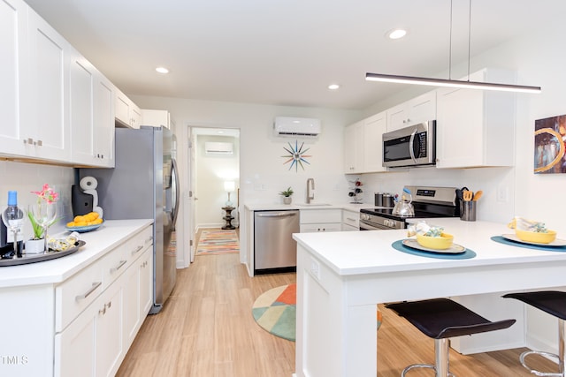 kitchen with stainless steel appliances, a peninsula, white cabinetry, light wood-style floors, and an AC wall unit