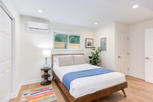 bedroom featuring light wood finished floors, electric panel, baseboards, a wall mounted AC, and recessed lighting