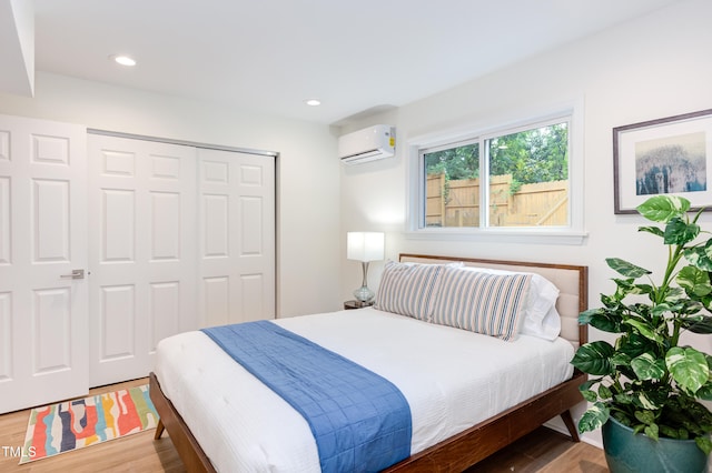 bedroom with a closet, a wall unit AC, wood finished floors, and recessed lighting