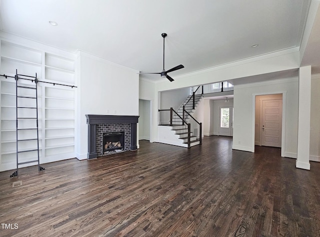 unfurnished living room featuring ceiling fan, a barn door, a tile fireplace, dark wood-style flooring, and stairway