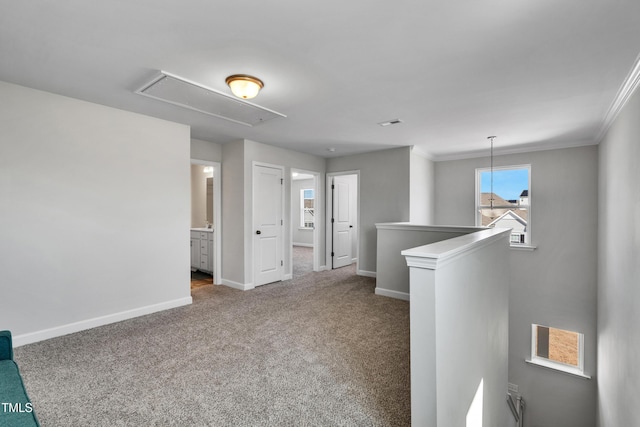 carpeted empty room featuring attic access, baseboards, and crown molding