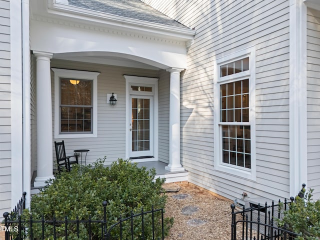 doorway to property with a shingled roof, covered porch, and fence