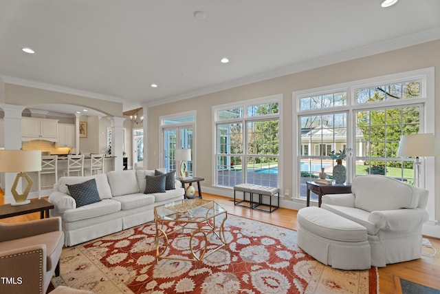 living room with arched walkways, light wood-style floors, ornamental molding, ornate columns, and recessed lighting