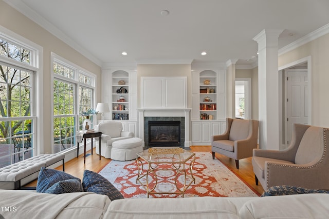 living room featuring light wood-style floors, built in features, and a tiled fireplace